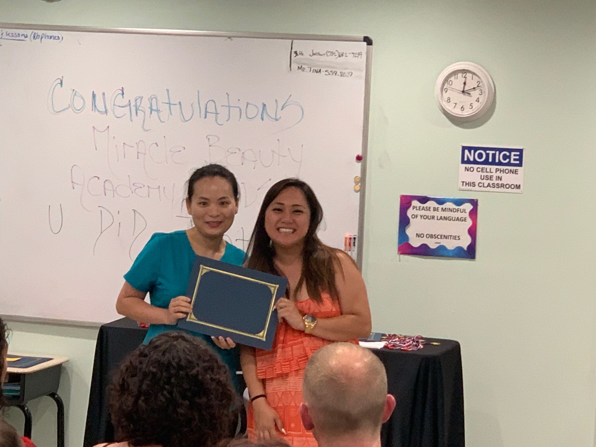 Two women are standing in front of a white board holding a certificate.