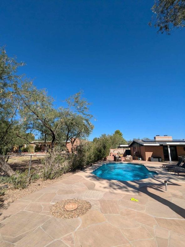 Backyard with a swimming pool and patio under a bright blue sky.