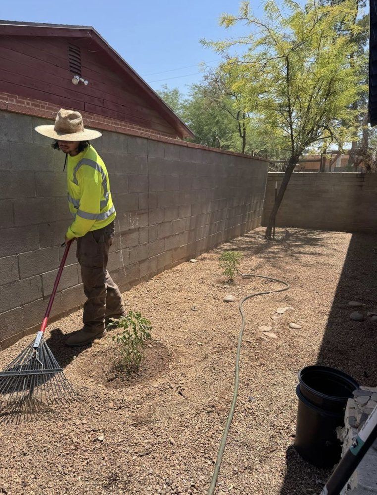 Person in reflective vest raking gravel in a yard next to a concrete wall.