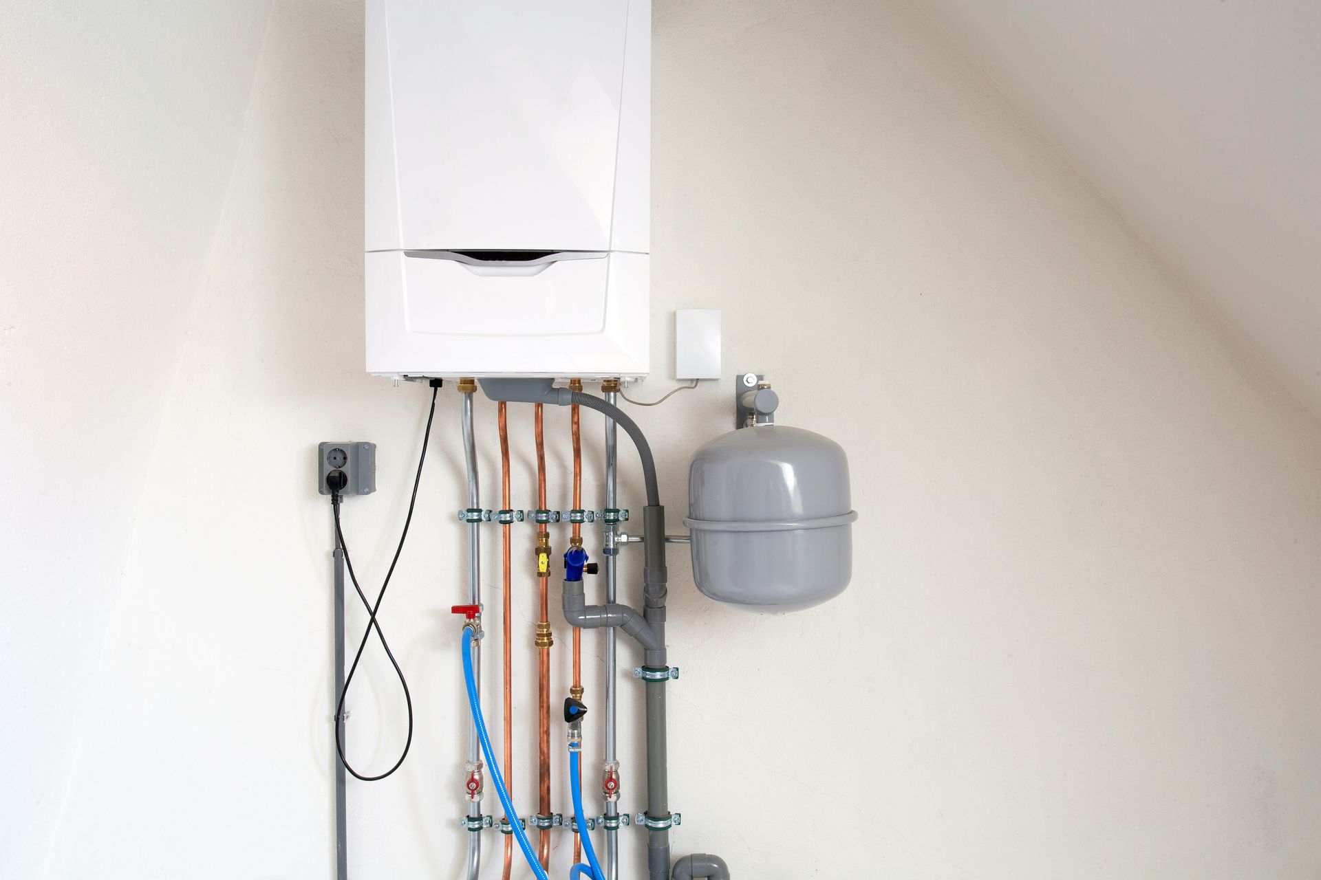 A white boiler is hanging on a wall next to pipes.