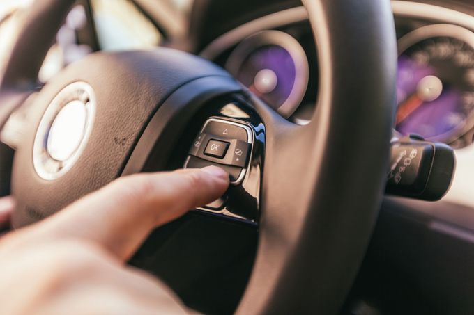 Il dito di una persona che preme un pulsante sul pannello di controllo del volante di un'automobile.