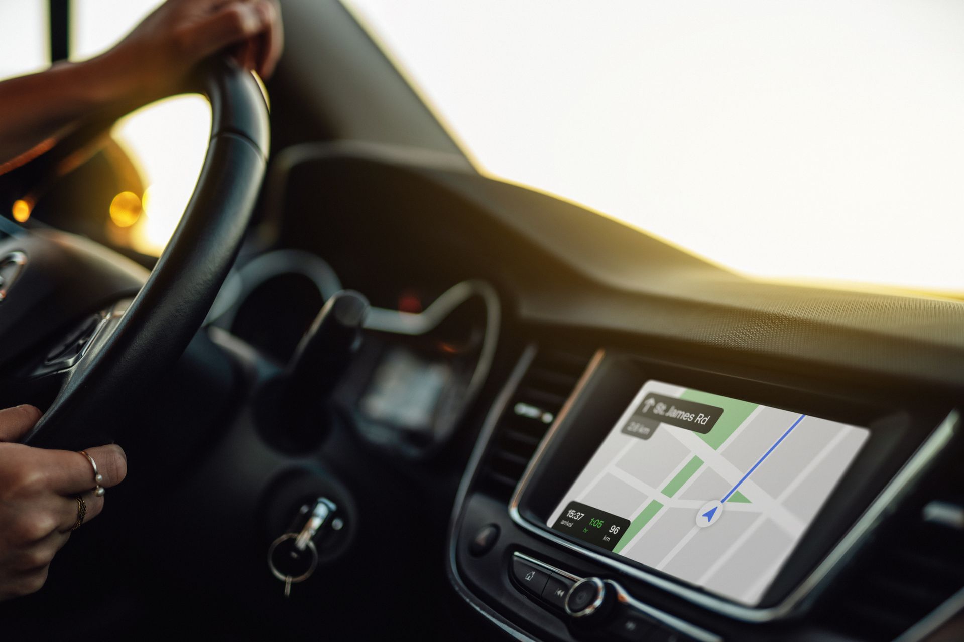 Le mani del conducente impugnano il volante di un'auto, mentre una mappa di navigazione digitale viene visualizzata sullo schermo del cruscotto.