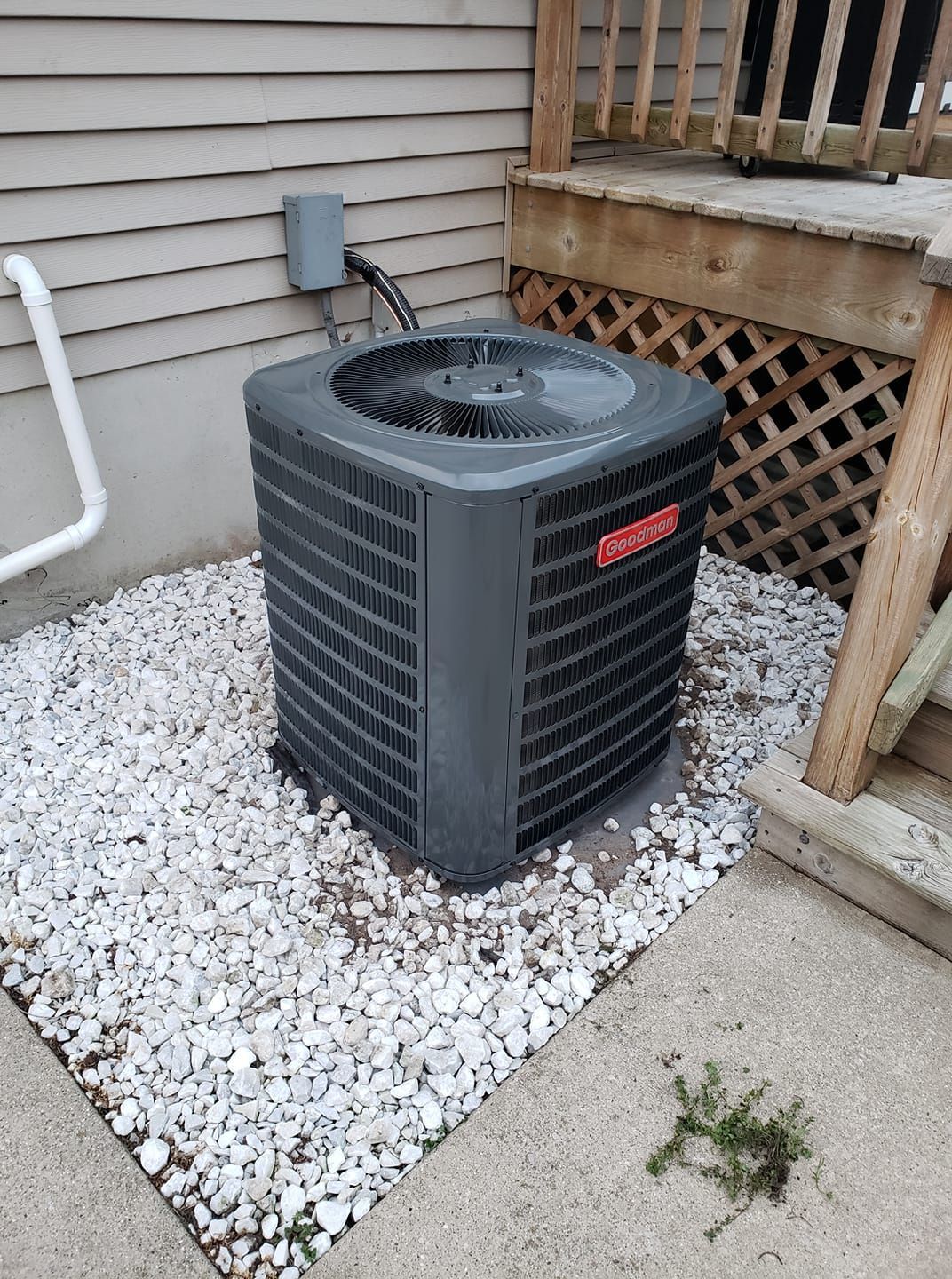 An air conditioner is sitting on top of a pile of gravel next to a house.