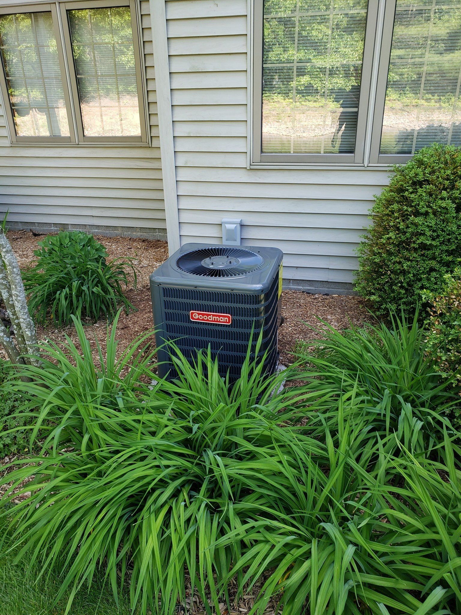 A black air conditioner is sitting in a garden next to a house.