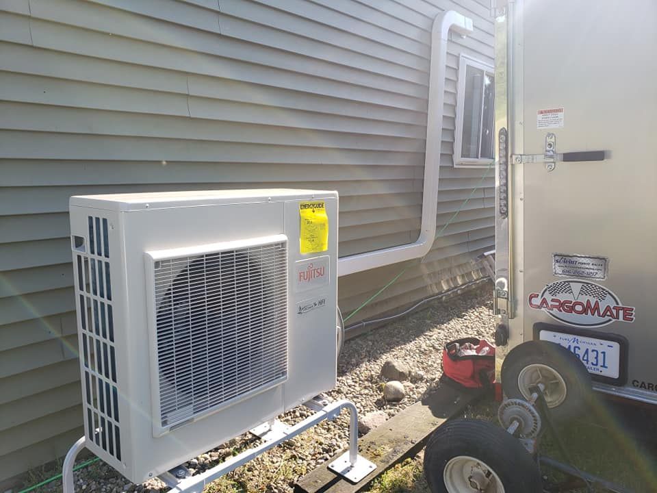 A white air conditioner is sitting on the side of a house next to a trailer.