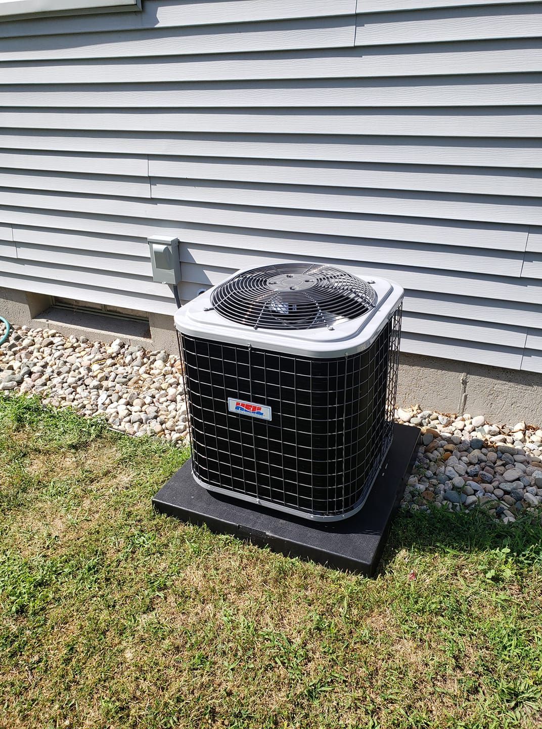 A black and white air conditioner is sitting in the grass in front of a house.
