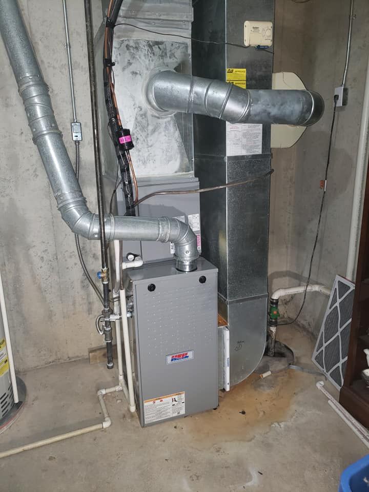 A furnace is sitting in a basement next to a pipe.