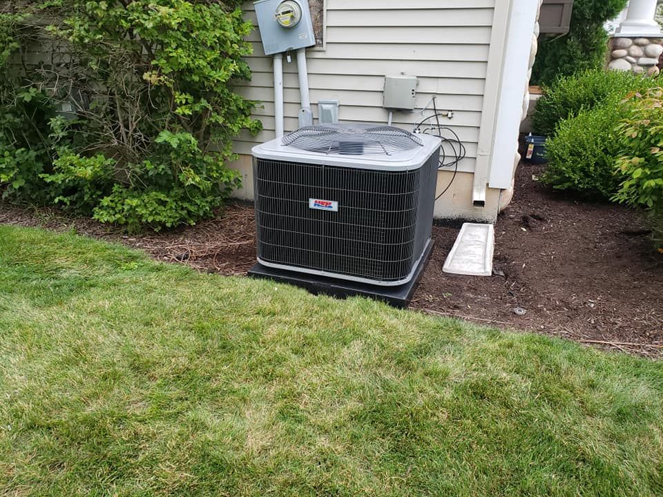 An air conditioner is sitting in the grass in front of a house.