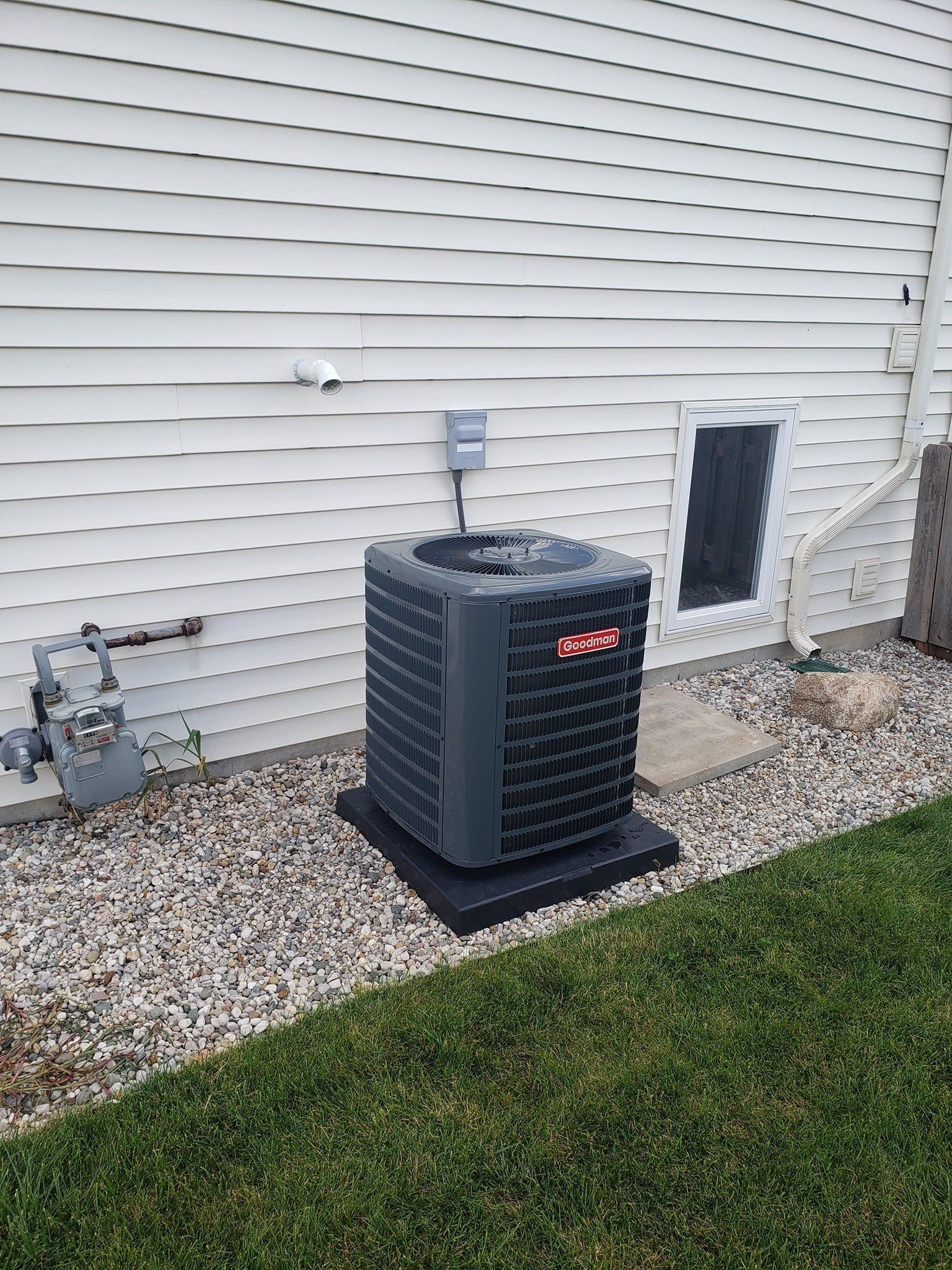 An air conditioner is sitting on the side of a house next to a window.