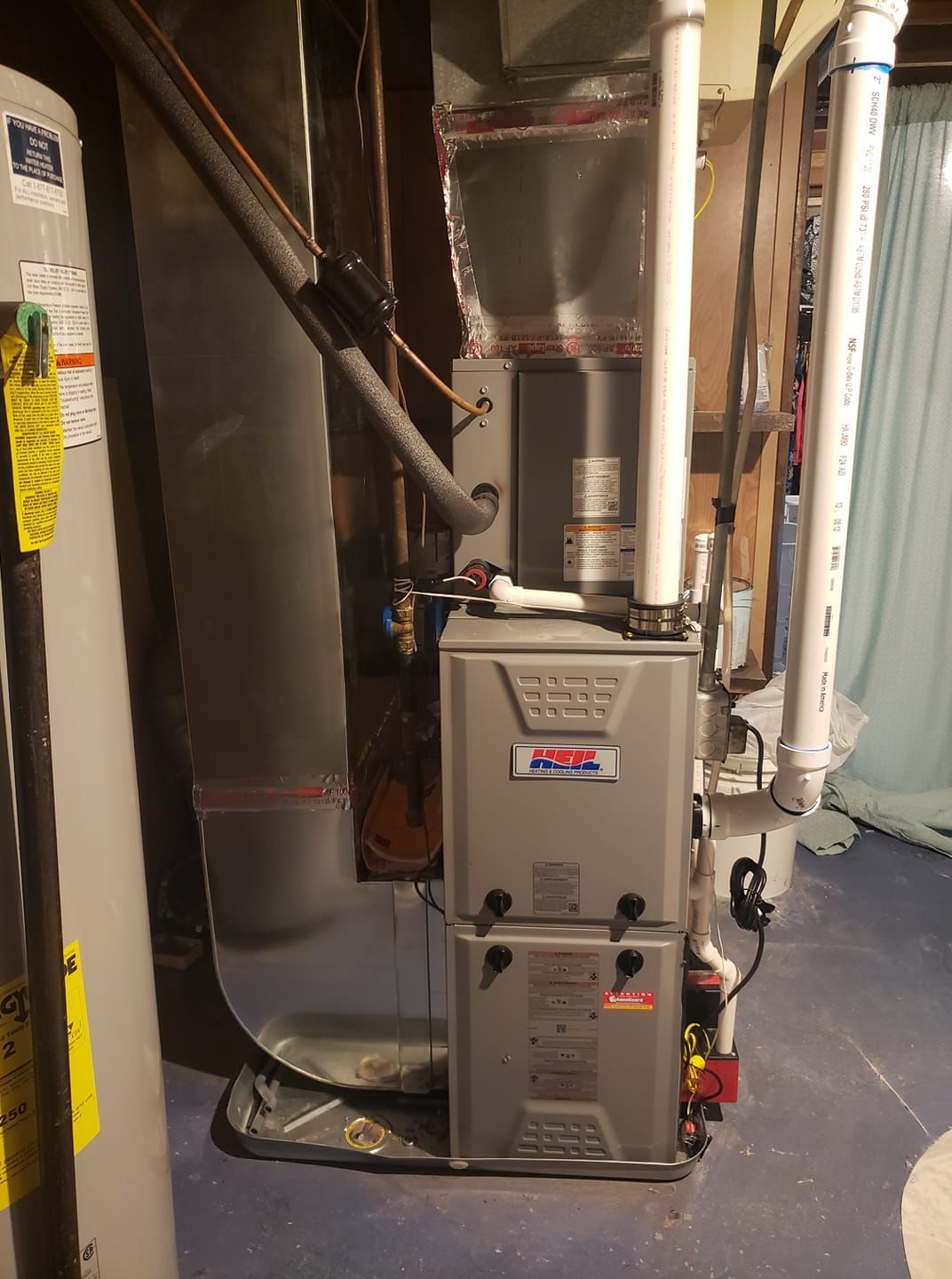 A furnace is sitting in a basement next to a water heater.