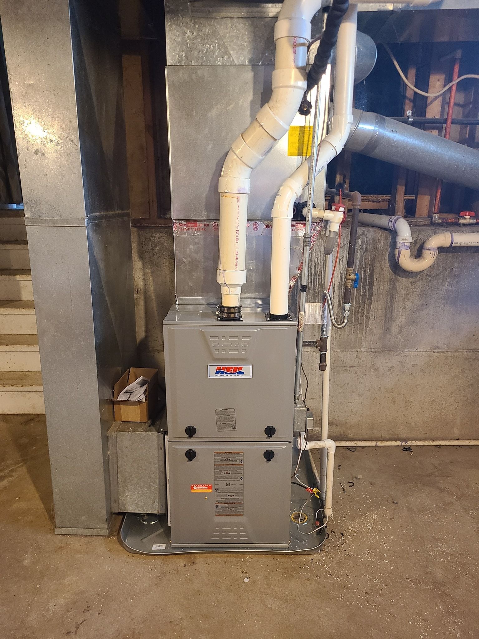 A furnace is sitting in a basement next to a wall.