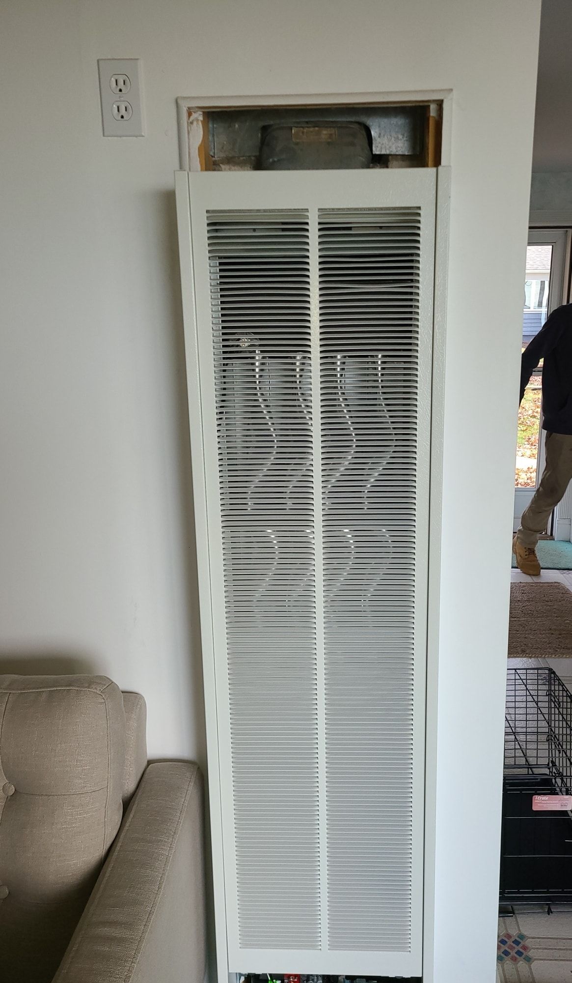 A white wall mounted heater is sitting in a living room next to a couch.