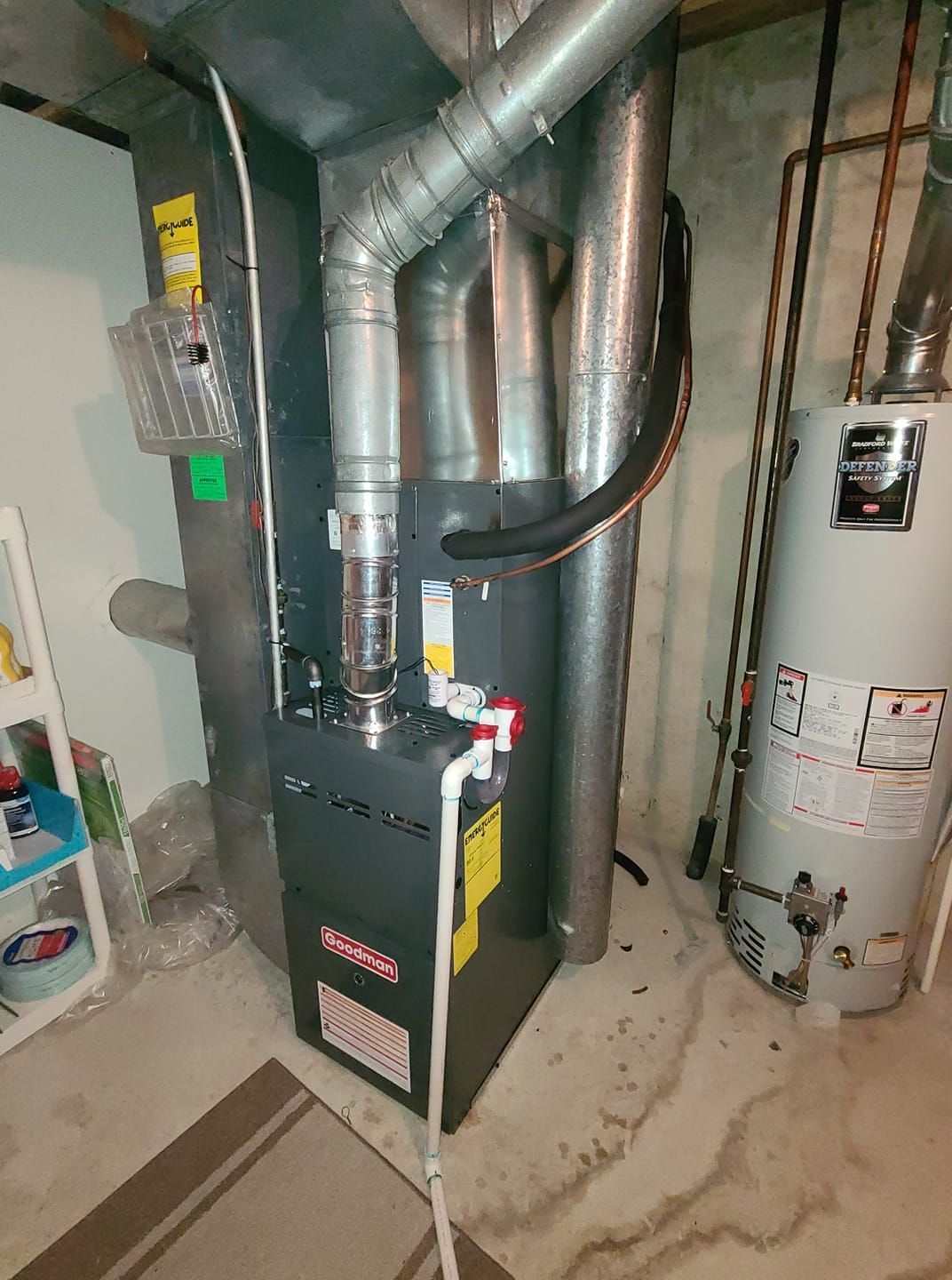 A gas heater is sitting in a basement next to a water heater.