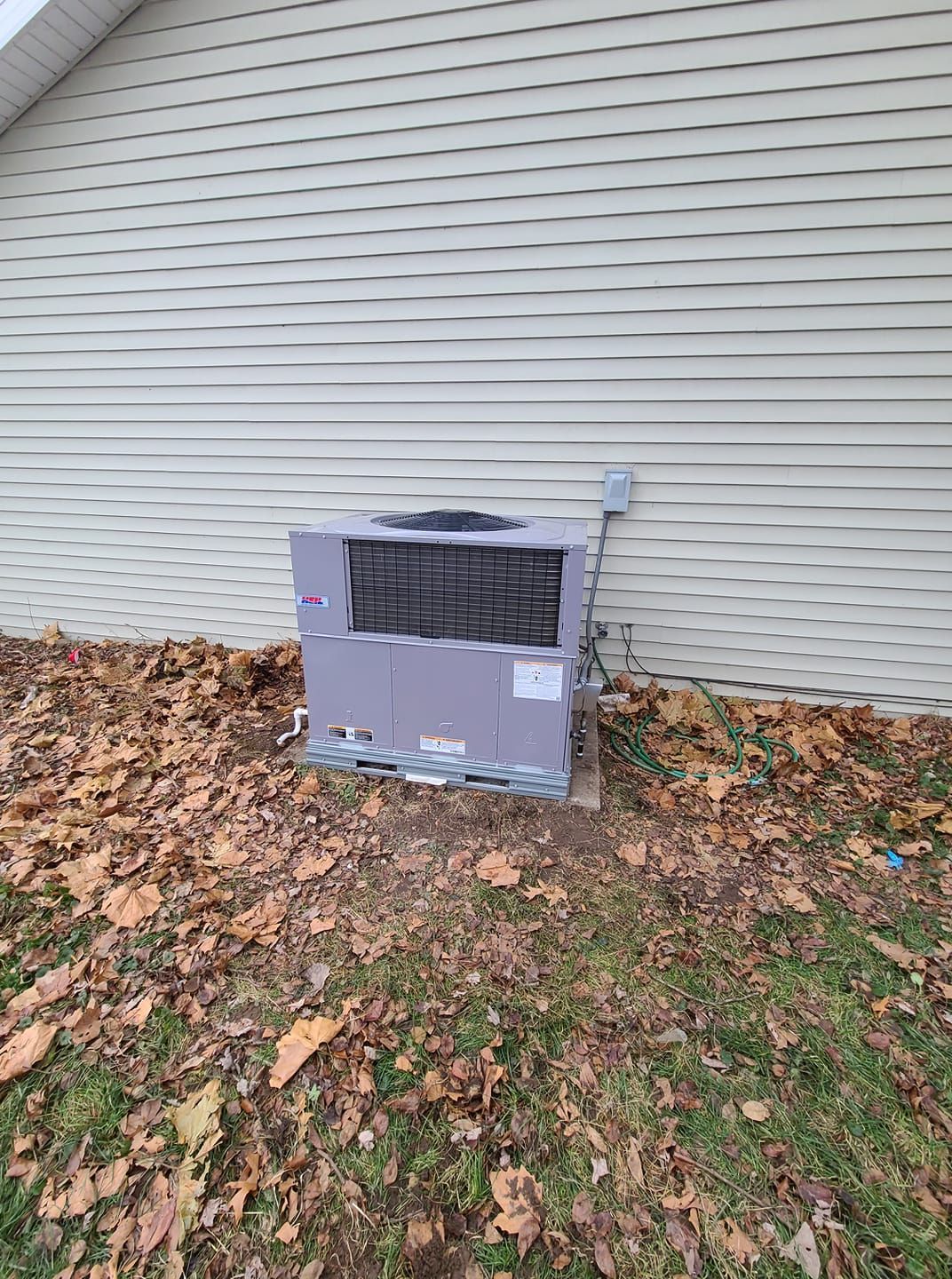 A gray air conditioner is sitting on the side of a house.