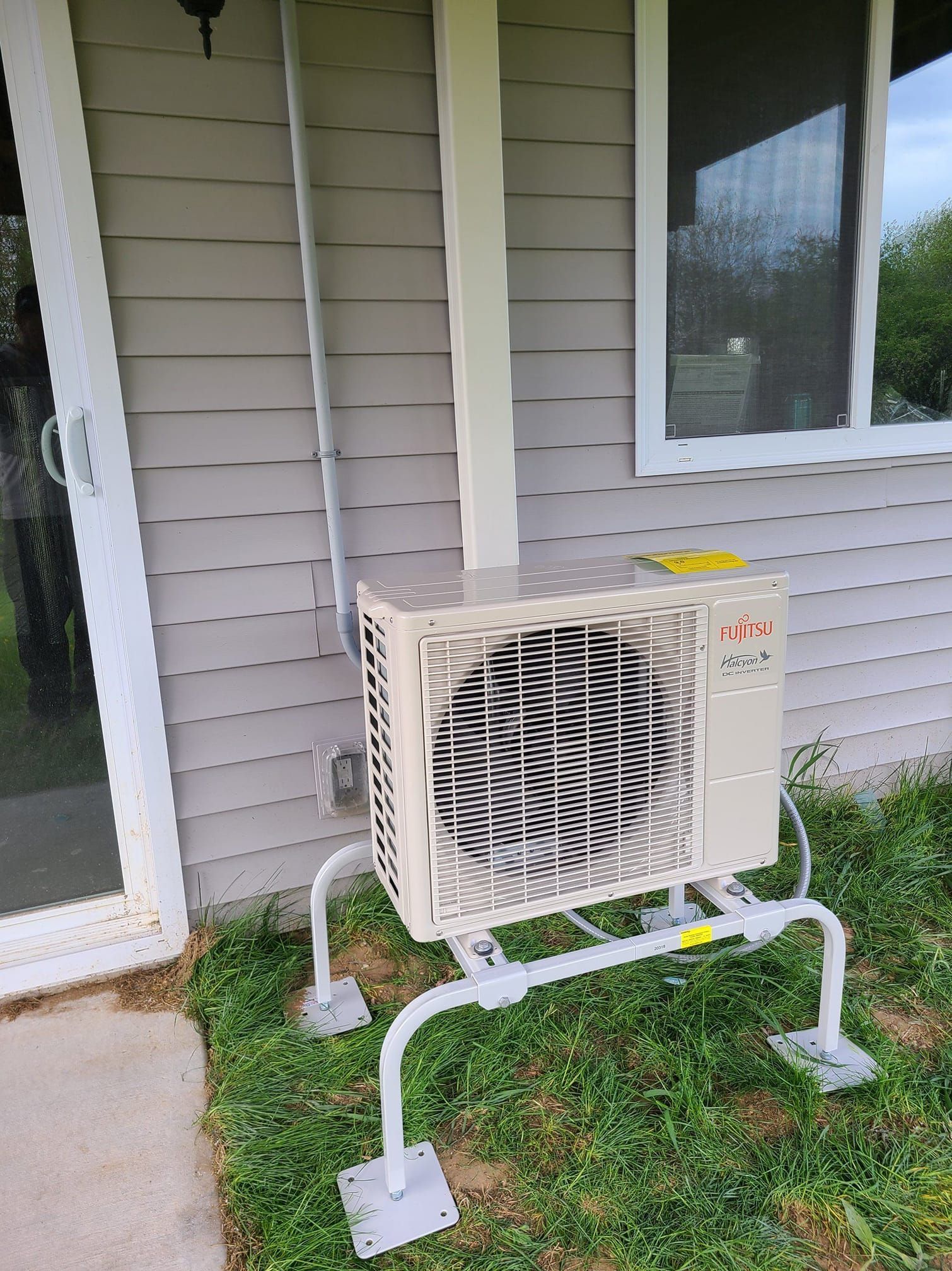 An air conditioner is sitting on the side of a house next to a window.