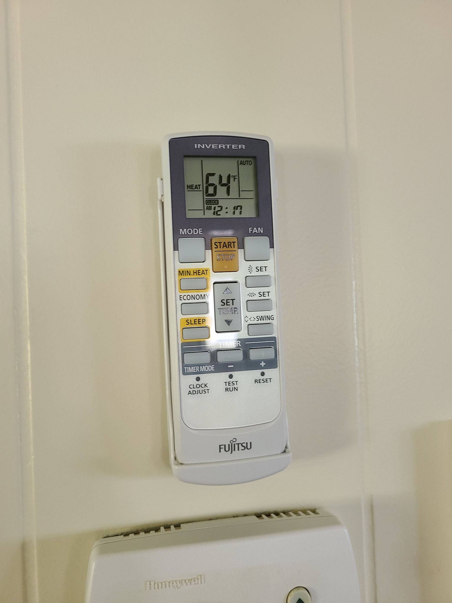 A remote control is hanging on a wall and shows the temperature as 64 degrees