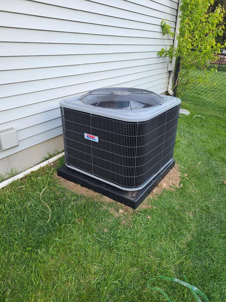 A black air conditioner is sitting in the grass next to a house.