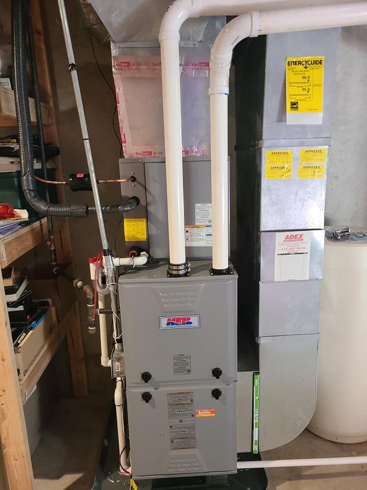 A furnace is sitting in a basement next to a water tank.