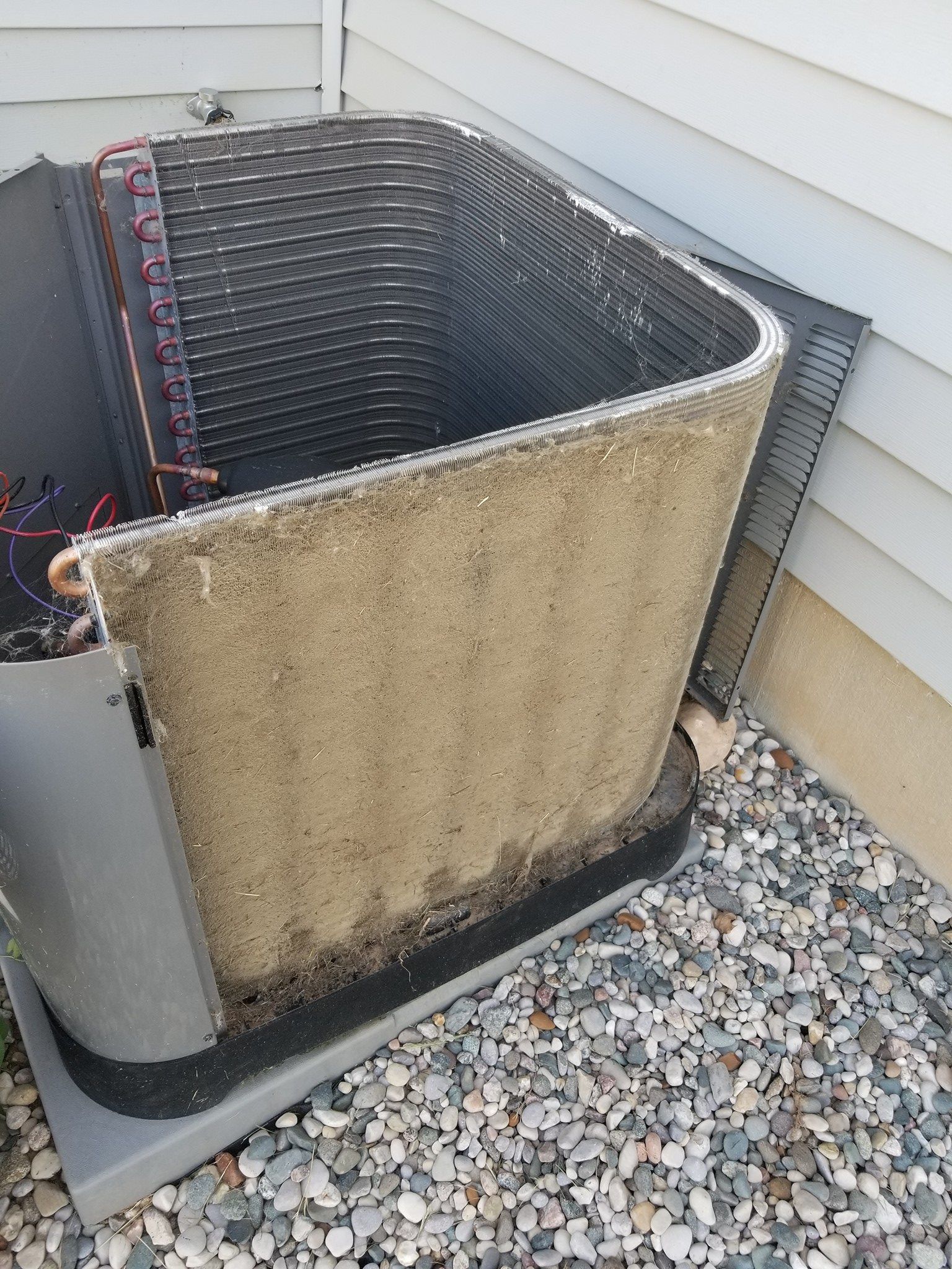 A dirty air conditioner is sitting on top of a pile of gravel next to a house.