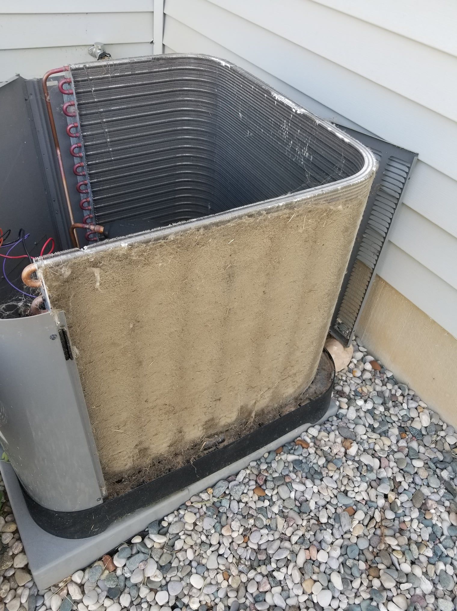A dirty air conditioner is sitting on top of a pile of gravel next to a house.