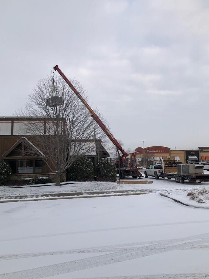 A crane is lifting a large object in the snow in front of a building