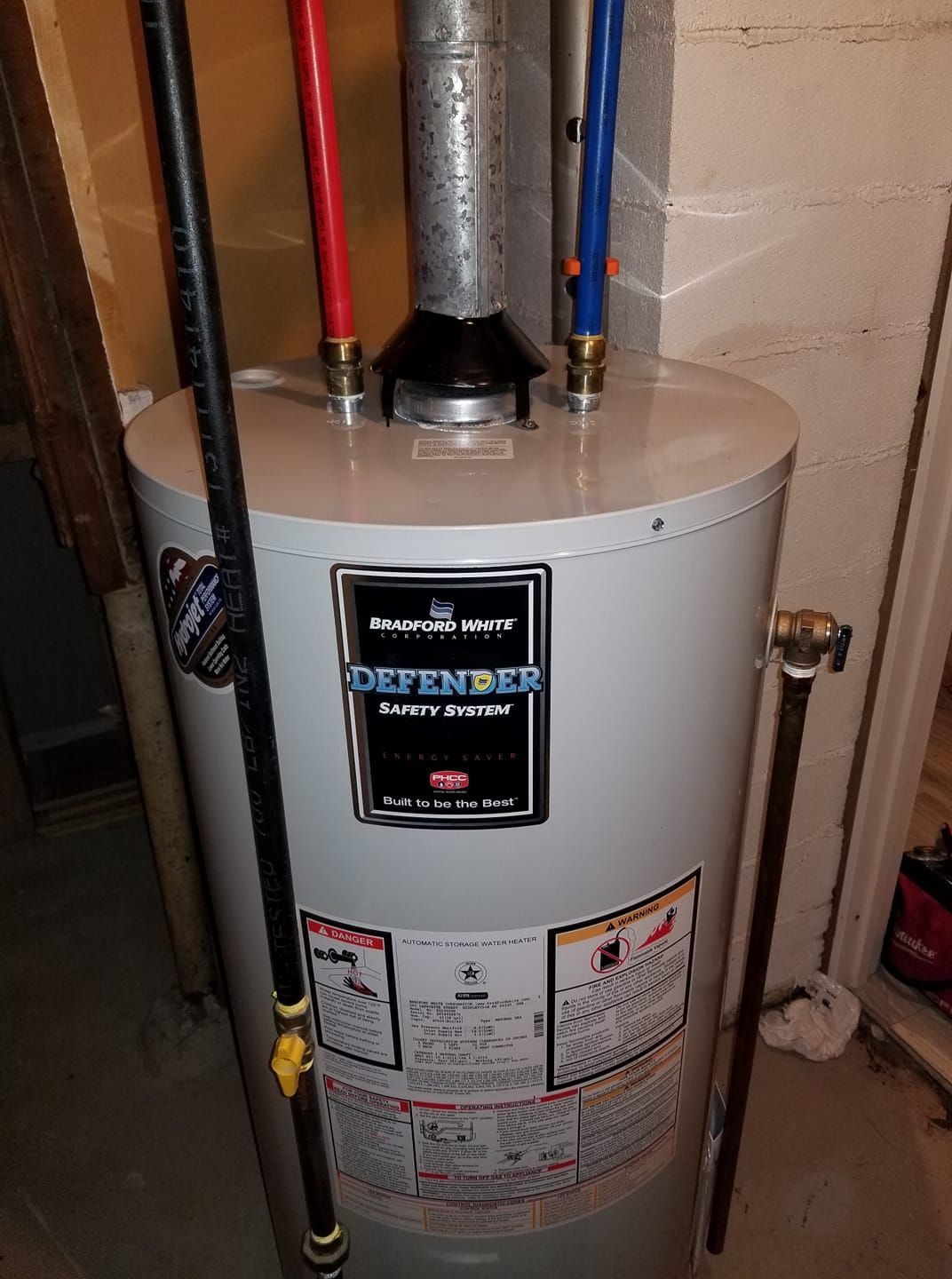 A water heater is sitting in a basement next to a wall.