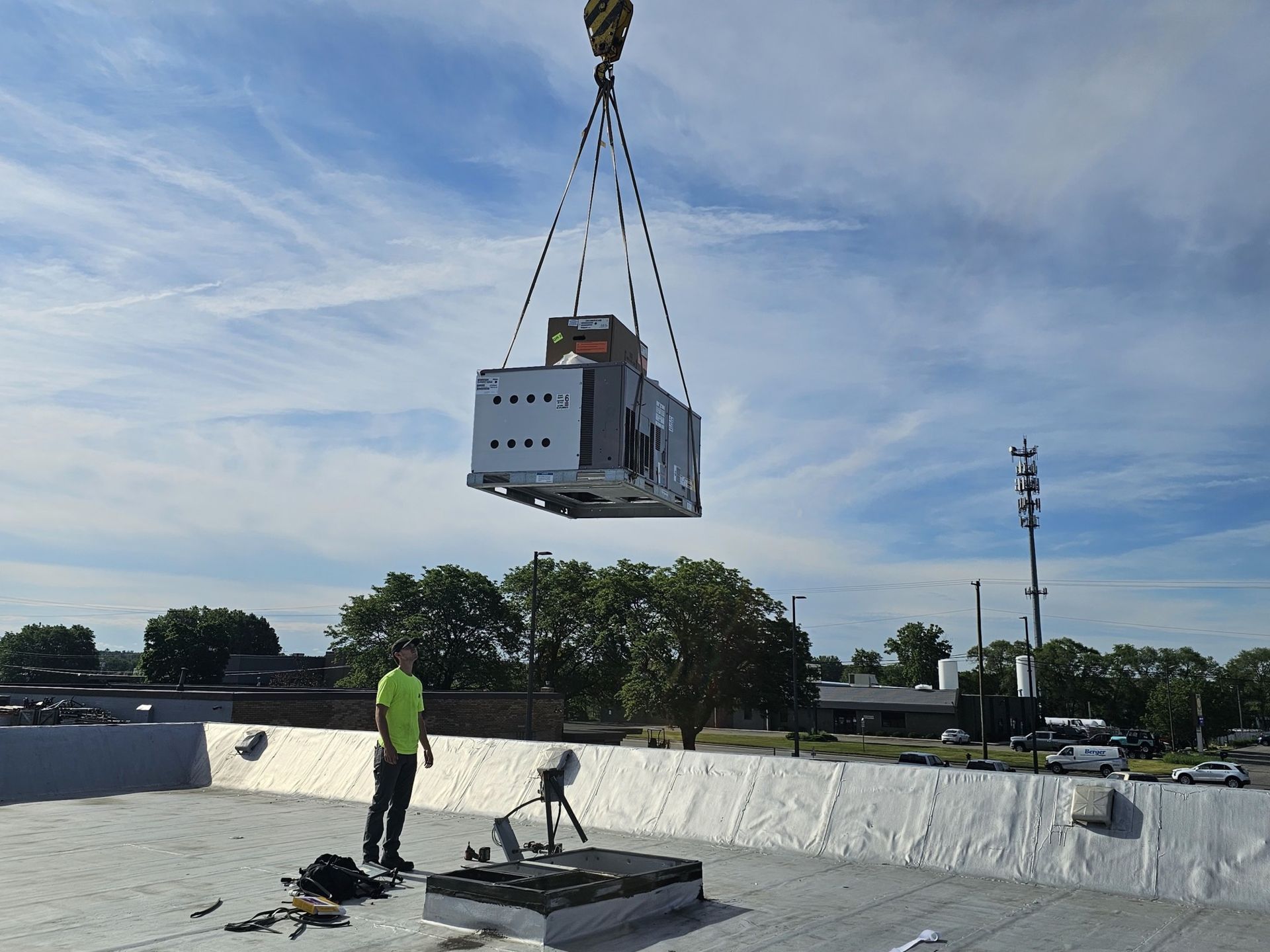 A man is standing on a roof watching a crane lift a large box into the air.