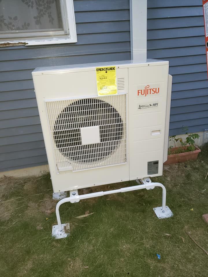 A fujitsu air conditioner is sitting outside of a house.