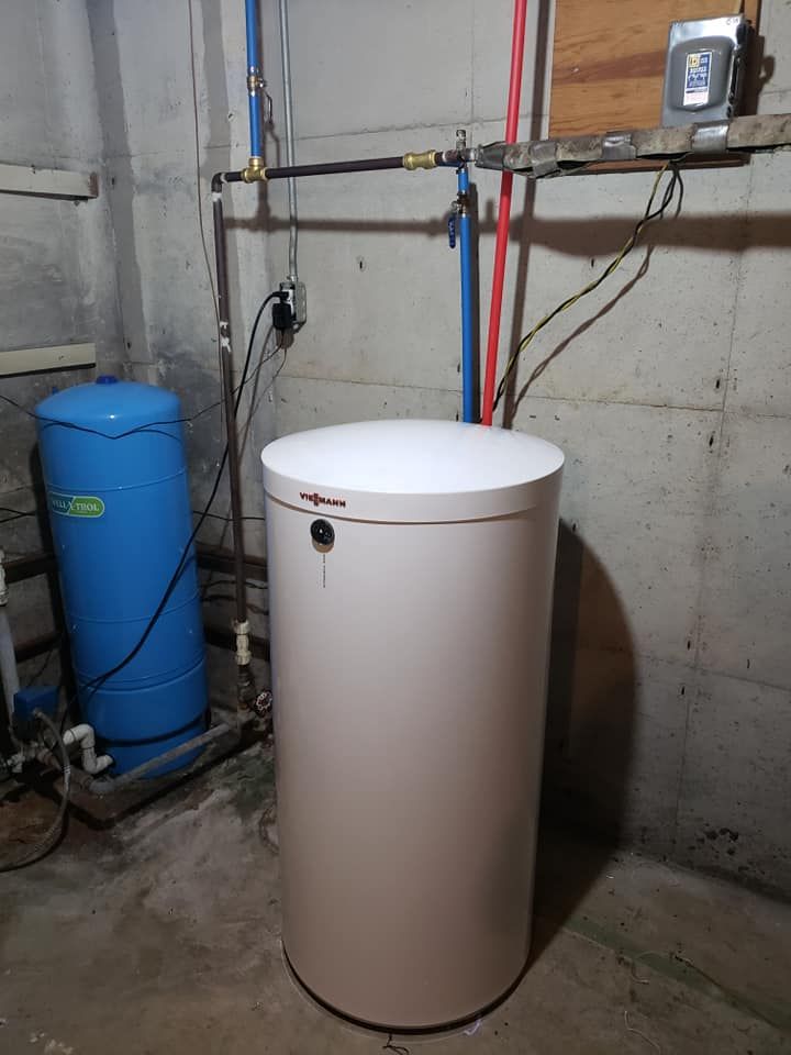 A white water heater is sitting in a basement next to a blue water tank.
