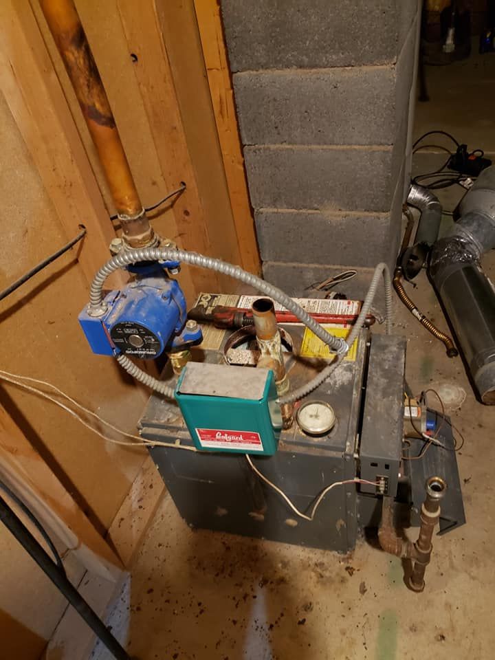 A boiler is sitting in a basement next to a chimney.