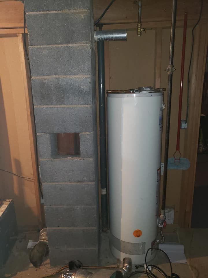 A water heater is sitting next to a chimney in a basement.