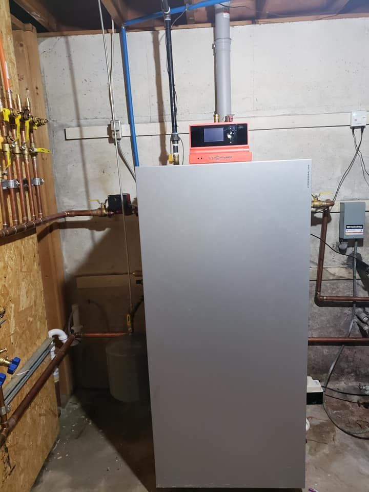 A large boiler is sitting in a basement next to pipes.
