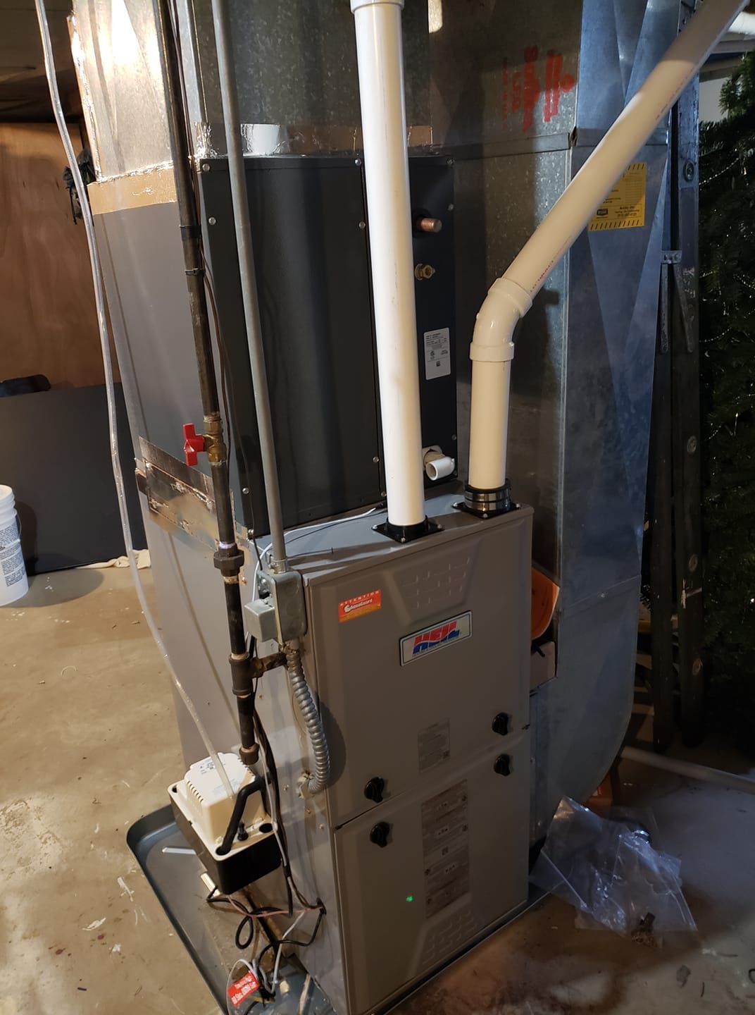 A furnace is sitting in a basement next to a pipe.
