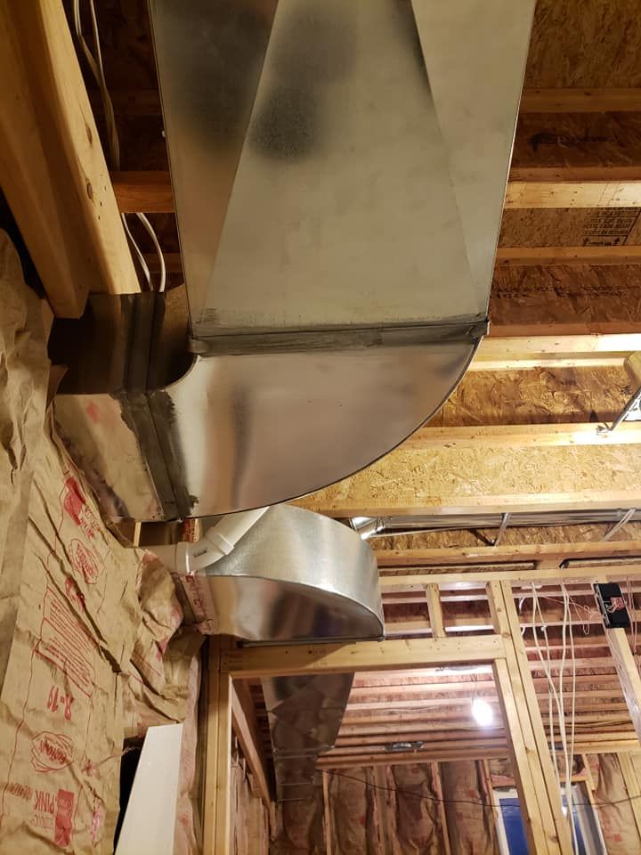 A metal duct is hanging from the ceiling of a house under construction.