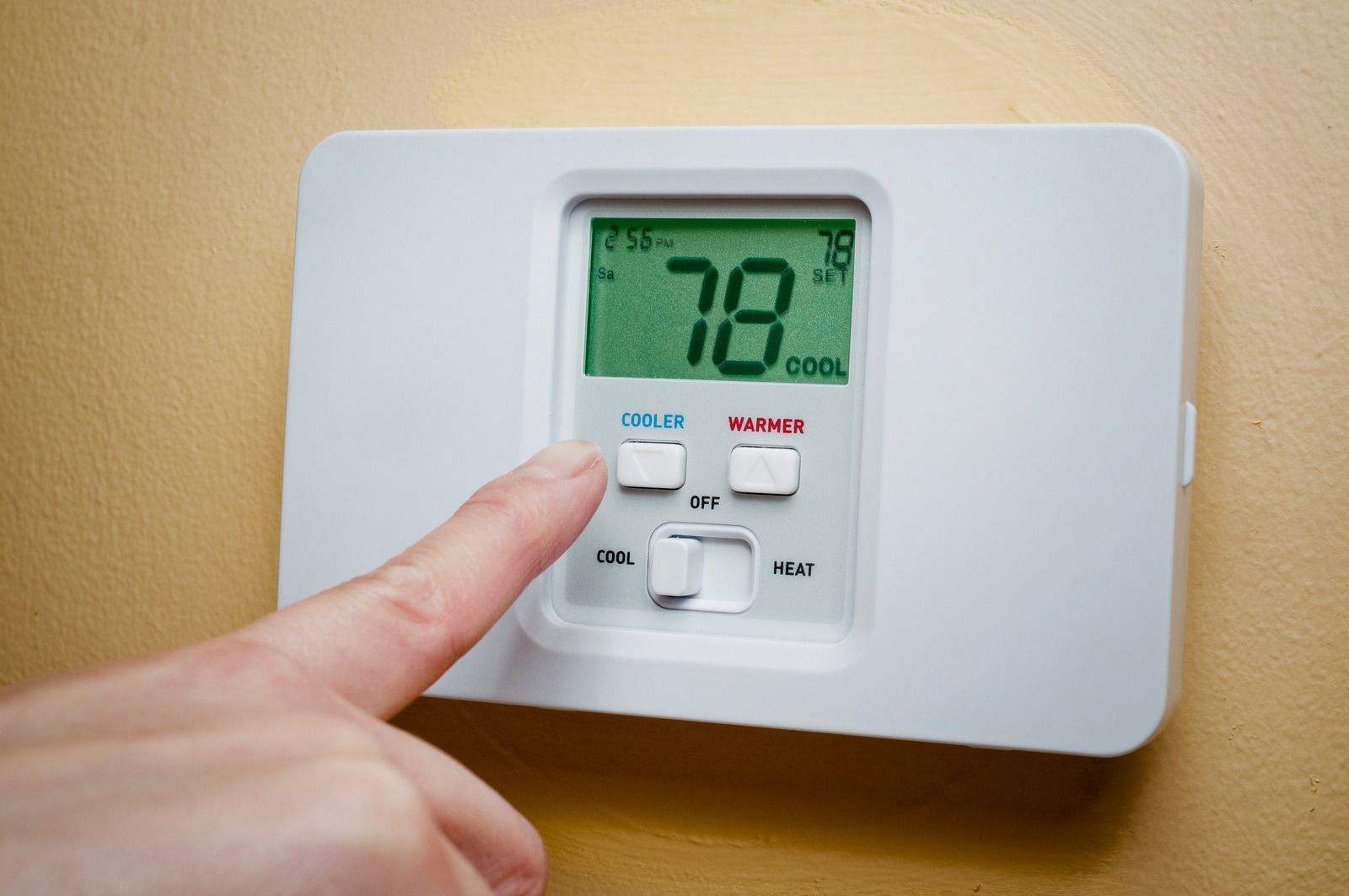 A person is pressing a button on a thermostat that is set to 78 degrees fahrenheit.