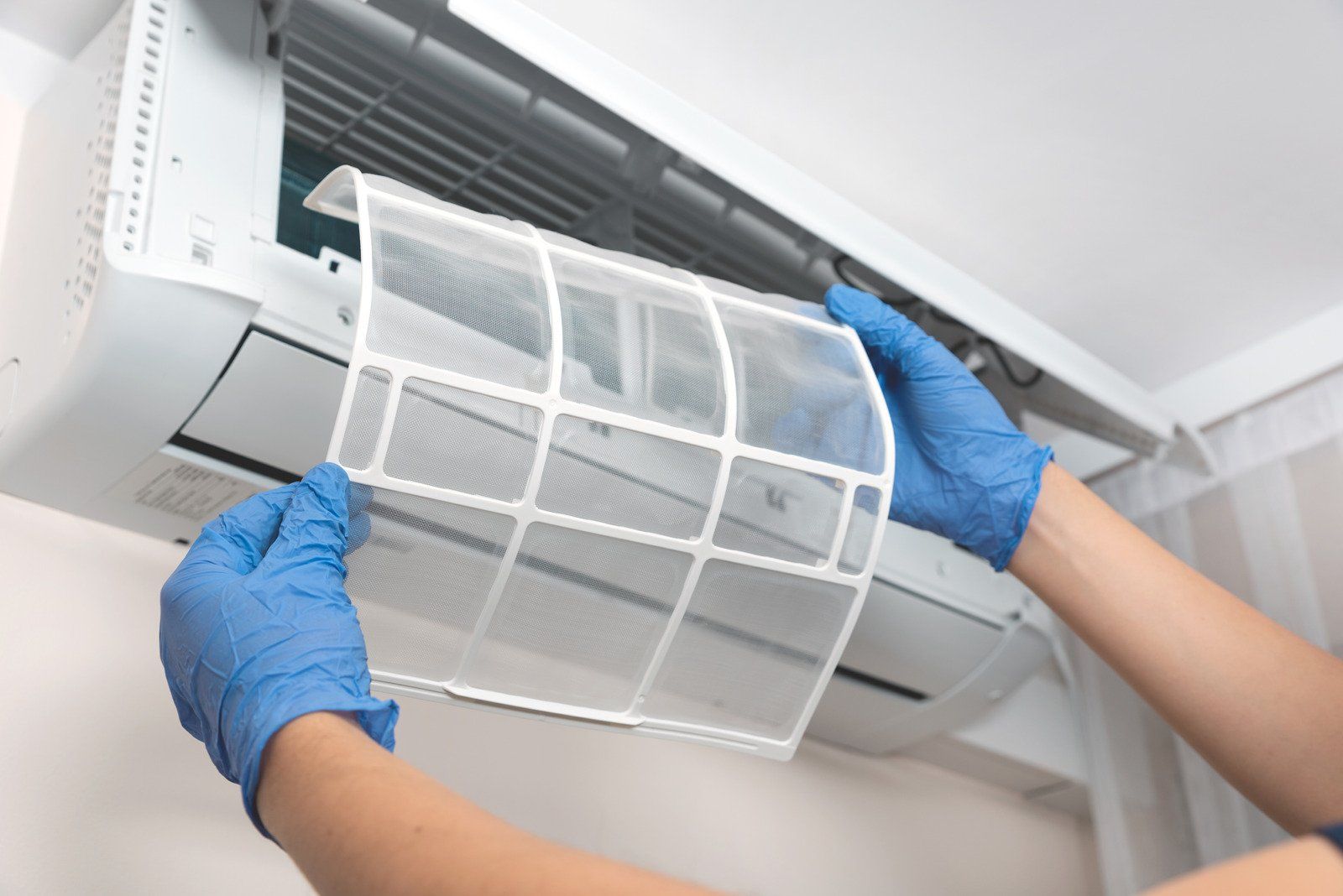 A person wearing blue gloves is cleaning an air conditioner.