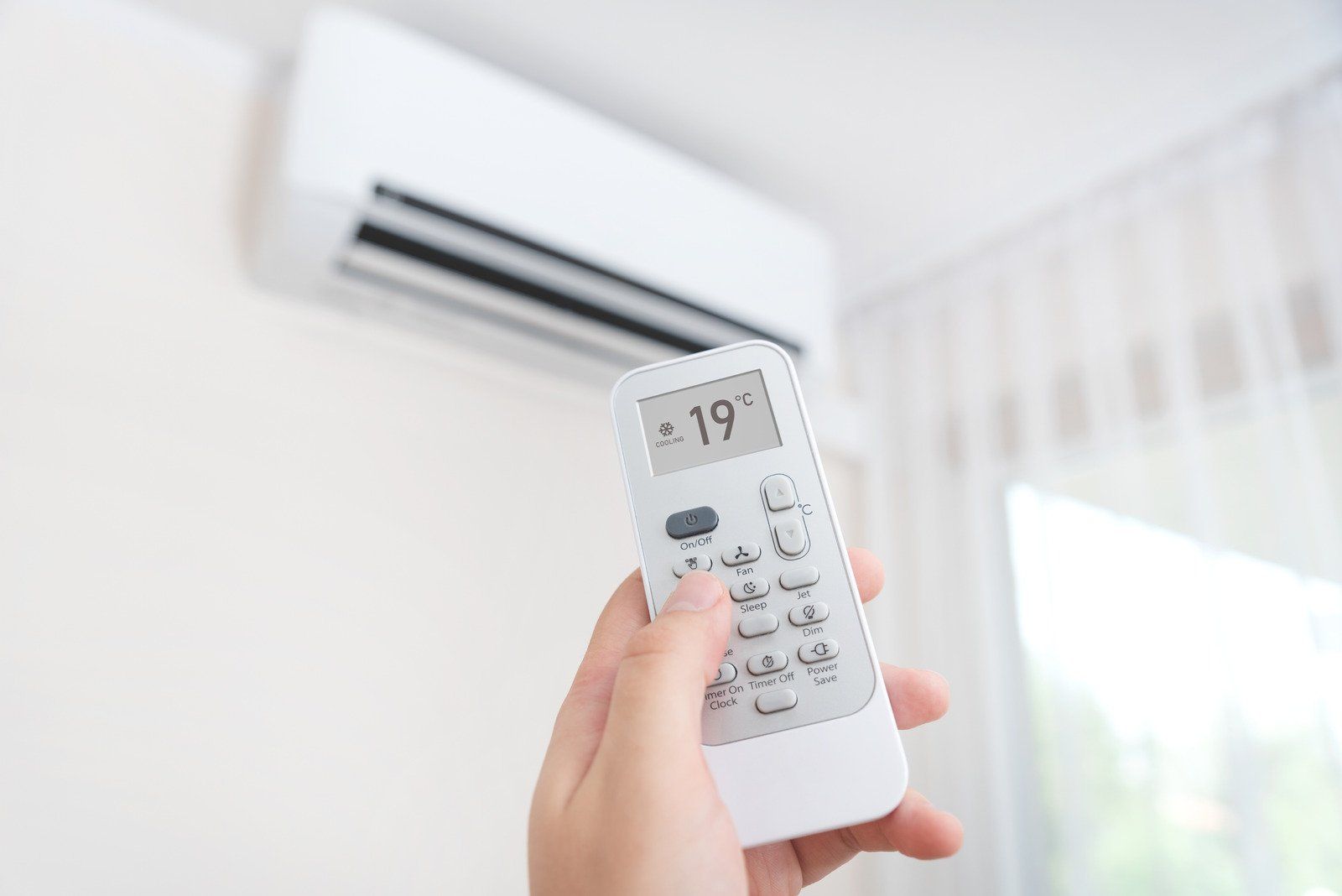 A person is holding a remote control in front of an air conditioner.