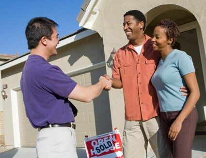 Couple shaking hands with estate agent outside their new home - Legal Service in Bloomington, IL
