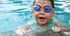 A young boy wearing goggles is swimming in a pool.