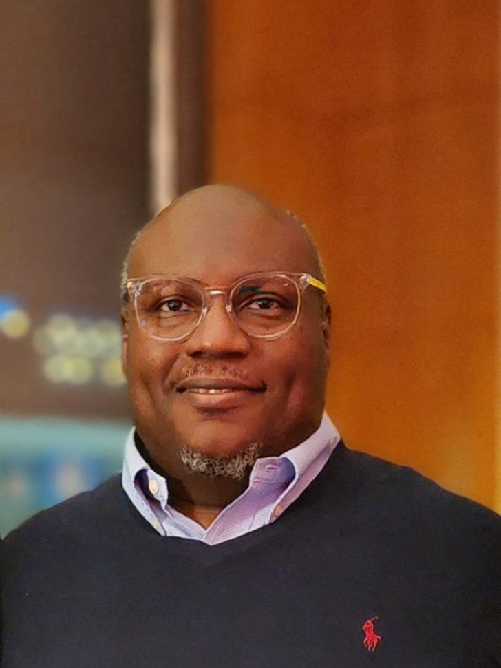A man wearing glasses and a blue sweater is smiling for the camera.