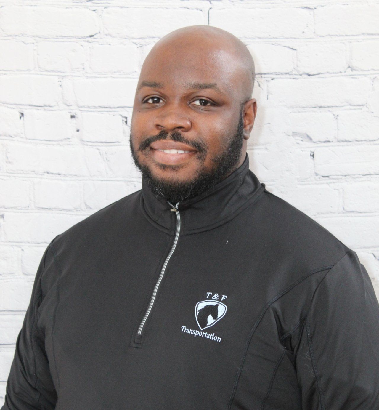 A bald man with a beard is wearing a black jacket with a shield on it.