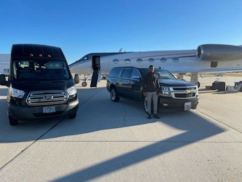 A man is standing next to a van and a suv in front of a private jet.