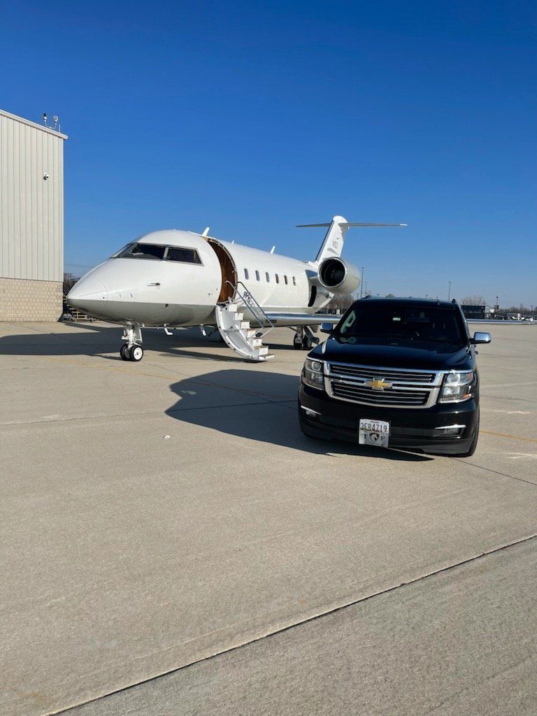 A car is parked next to a private jet on a runway.