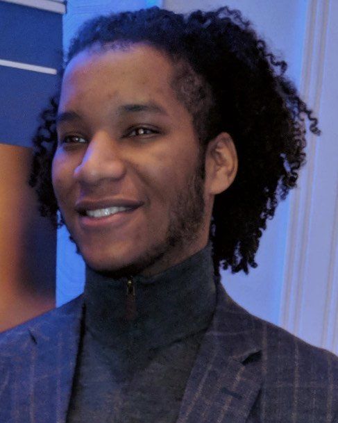A man with curly hair is wearing a suit and smiling