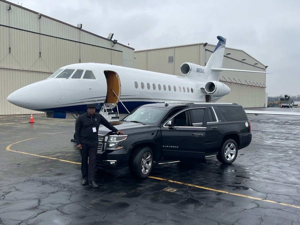 A man is standing next to a car in front of a private jet.