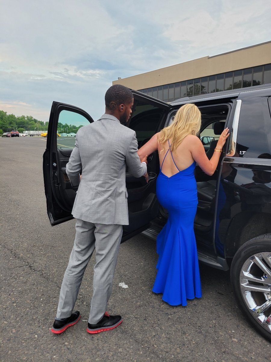 A man in a suit is helping a woman in a blue dress get out of a car.