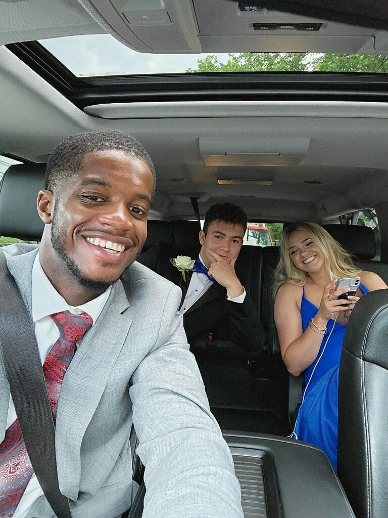 A man in a suit and tie is taking a selfie in the back seat of a car.