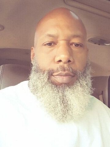 A bald man with a beard is sitting in a car.