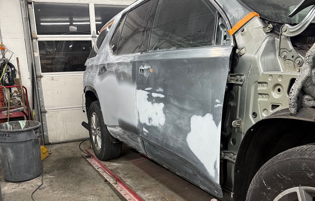 A damaged car with sanded body filler on its side panel is being repaired inside a garage workshop. | Big n' Littles Auto Body