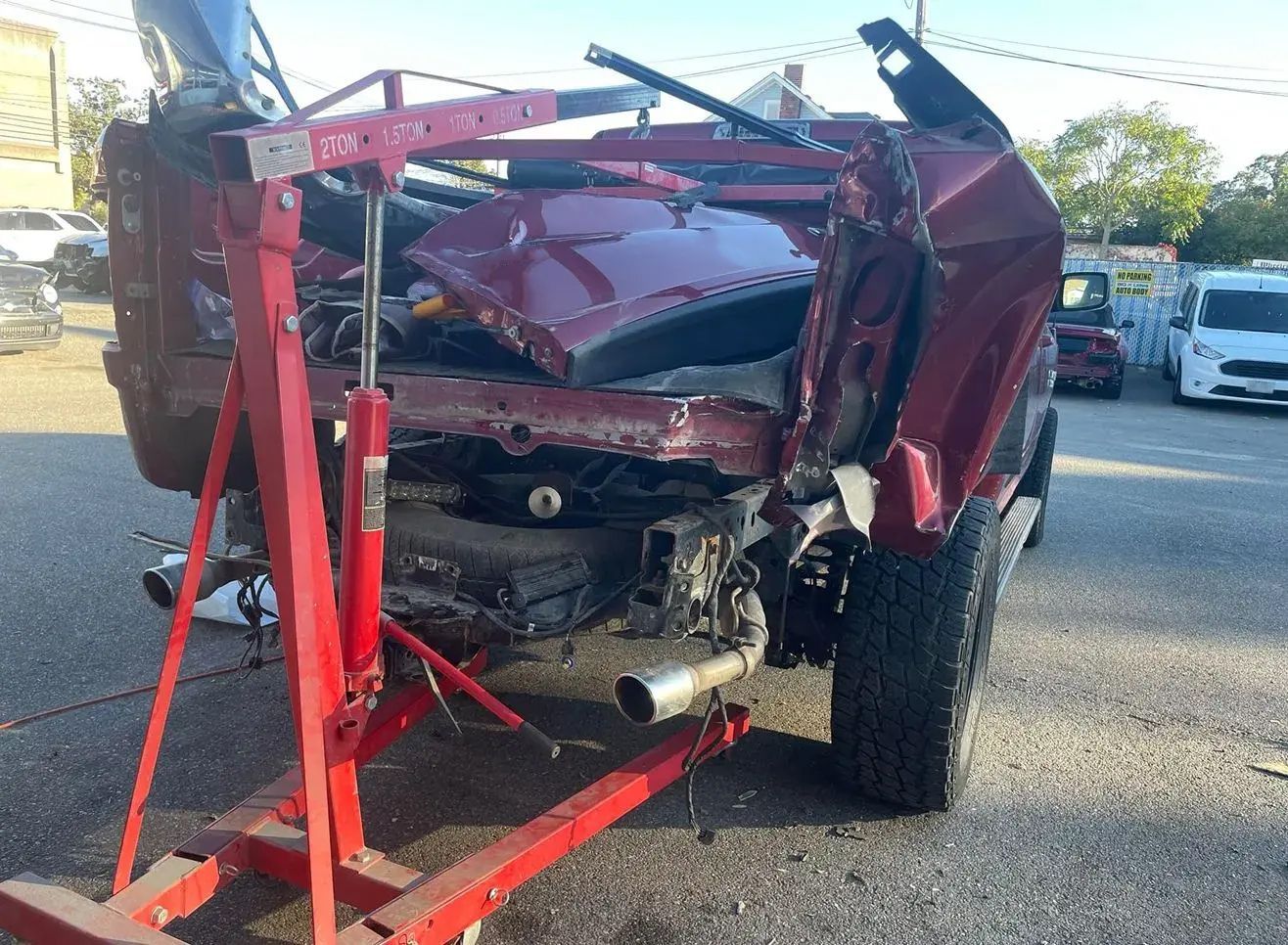 Red pickup truck severely damaged, rear end crushed. Being lifted by a red engine hoist, in a parking lot. | Big n' Littles Auto Body